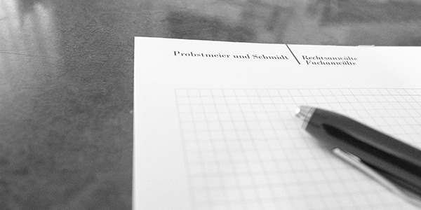 Schwarz-weiß Foto eines karierten Papiers und eines Stifts auf einem Tisch.